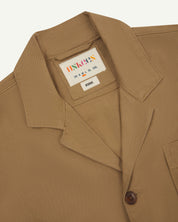 Front flat close up shot of uskees men's khaki organic cotton jacket showing front button fastening and  brand label at neck