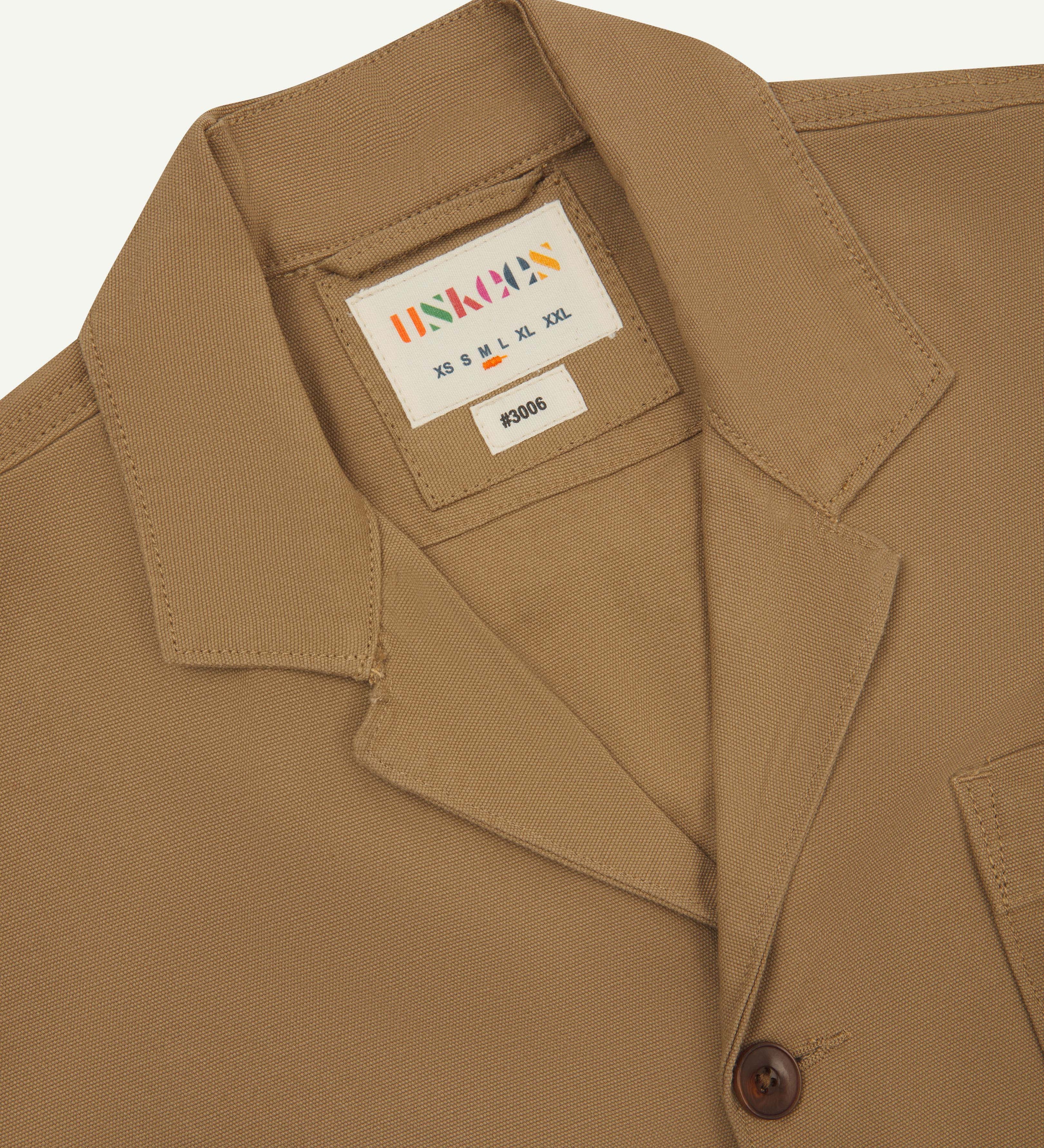 Front flat close up shot of uskees men's khaki organic cotton jacket showing front button fastening and  brand label at neck