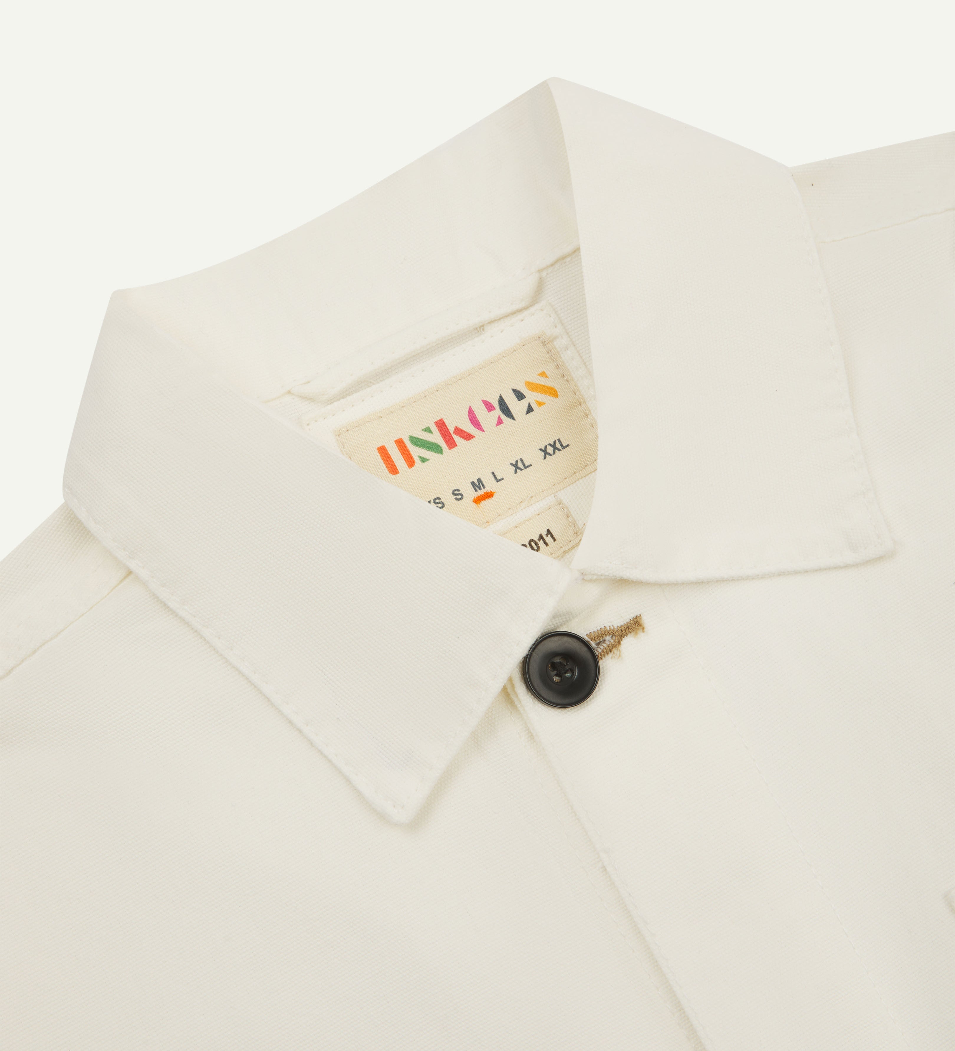 Close-up, top-half front view of cream overshirt showing collar and with top button fastened and Uskees label