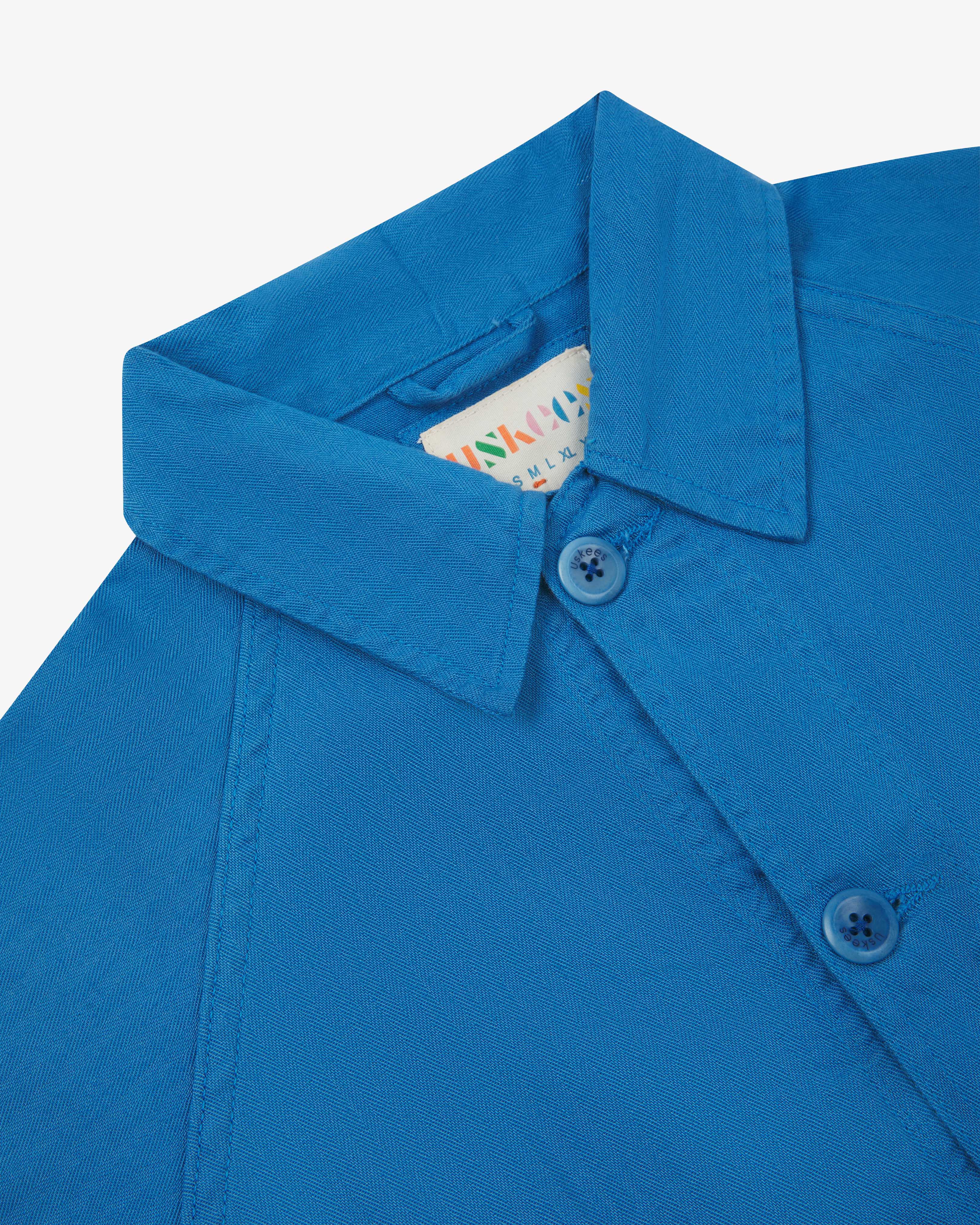 Neck view of Uskees 3041 opal-blue herringbone cotton signal jacket with focus on collar, Uskees brand label and matching corozo buttons.