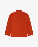 Back view of rust-red, buttoned corduroy overshirt with view of reinforced elbow area and boxy silhouette.