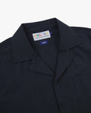 Front close up shot of an Uskees dark blue, button front, short sleeve shirt showing the collar and brand label at neck.