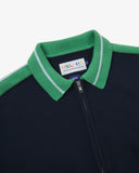 Close up view of an Uskees navy and green tracksuit top with green collar and front zipper, featuring a visible brand logo.