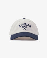 Cream baseball cap with navy peak and 'USKEES' logo on front, presented on a white background