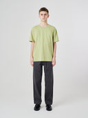 Male model wearing an Uskees light green t-shirt and black pants on a white background