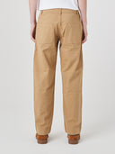 Back view of the bottom half of a male model wearing beige Uskees painter pants and brown shoes, presented on a white background