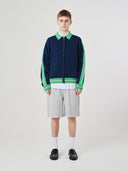 Male model wearing a navy and green track jacket with light gray shorts on a white background