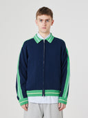 Male model showing top half wearing an Uskees navy and green track jacket with light gray shorts on a white background