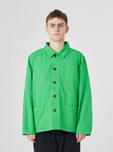 Front model shot of Uskees organic cotton bright green shirt-jacket with dark blue trousers, presented on a light gray background