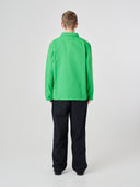 Back shot of a male model wearing Uskees organic cotton bright green shirt-jacket and dark blue trousers, presented on a light gray background