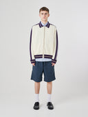 Male model wearing a cream track jacket with light blue shorts on a white background