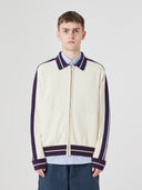 Top half of male model wearing an Uskees cream track jacket with light blue shorts 