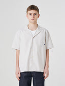 Male model wearing an Uskees ecru short sleeve, button front shirt and dark blue orta denim jeans on a white background