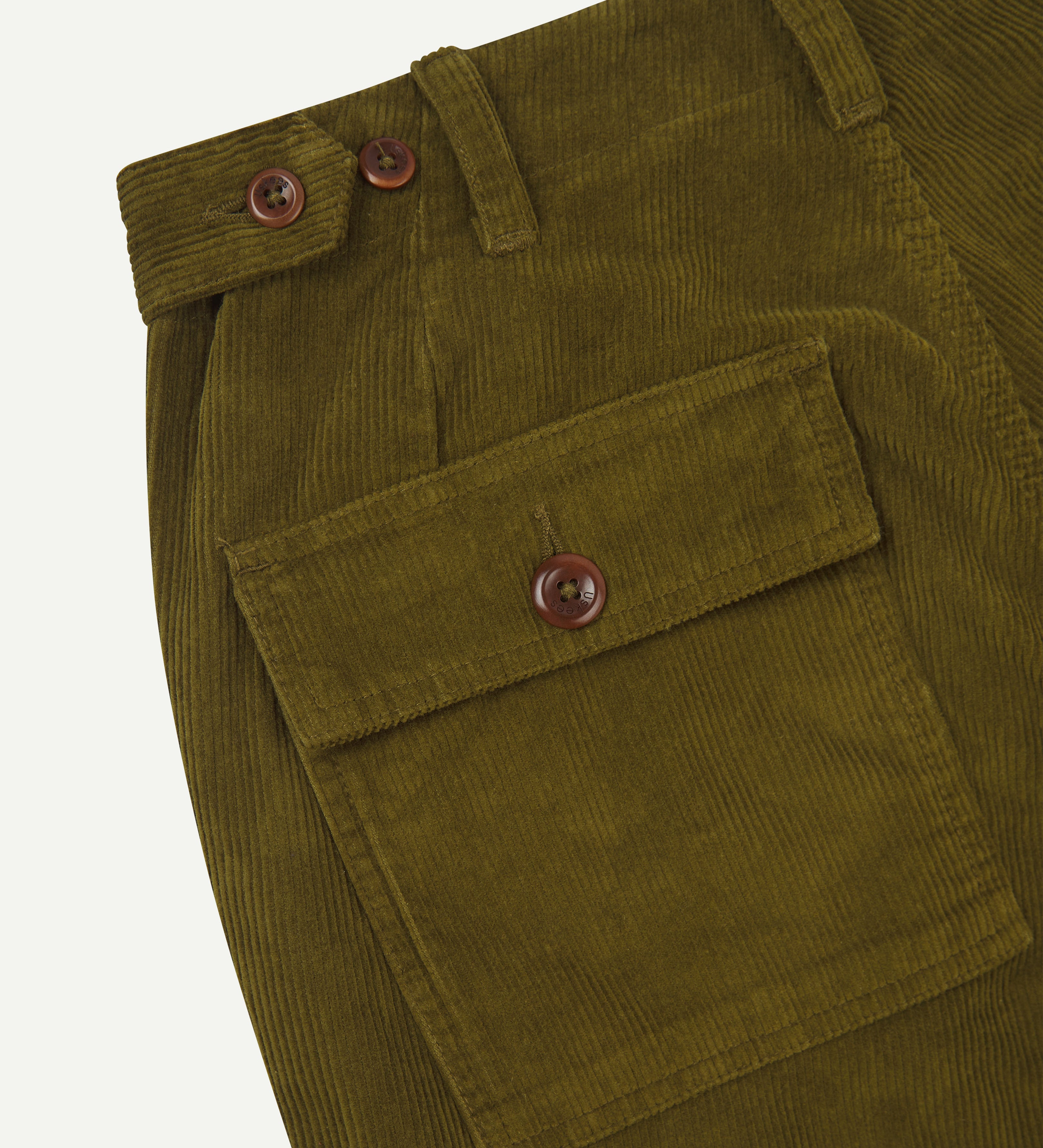 Close-up of green corduroy pants with a buttoned back pocket and waist adjuster buttons on a white background