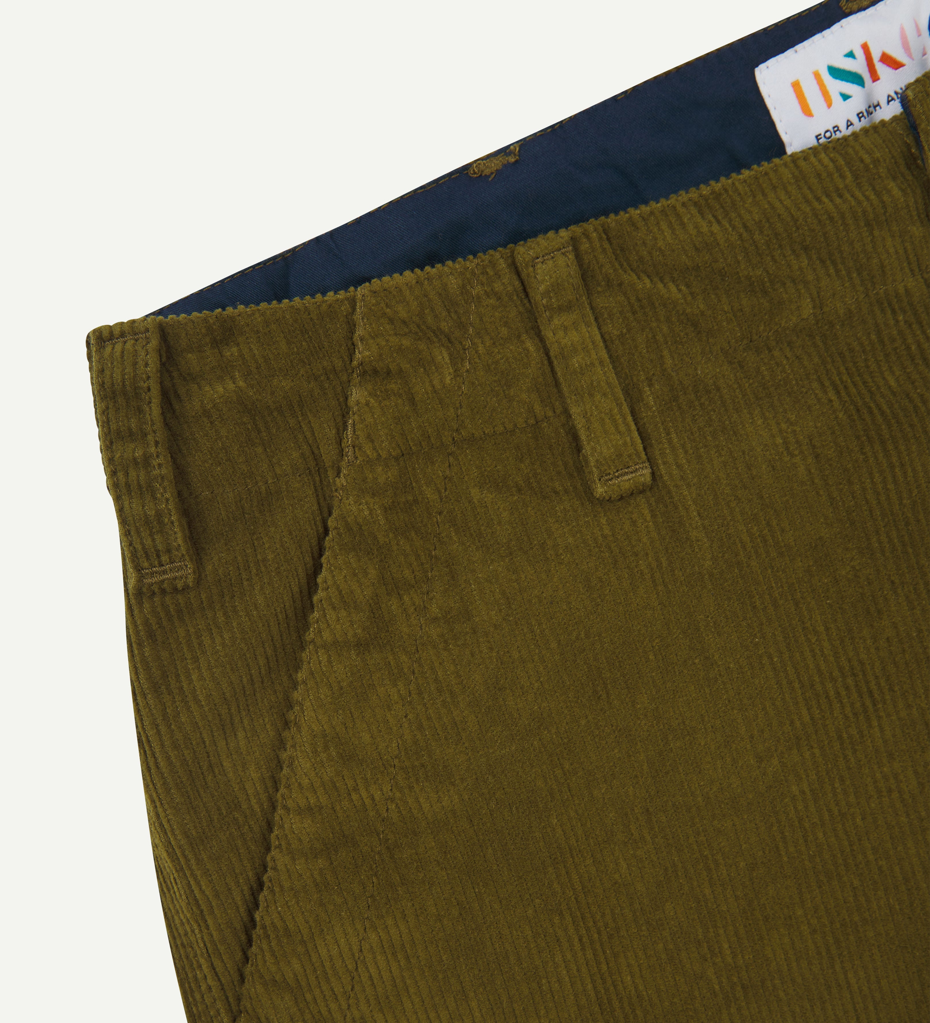 Close-up of green corduroy pants with a visible Uskees brand label on a white background