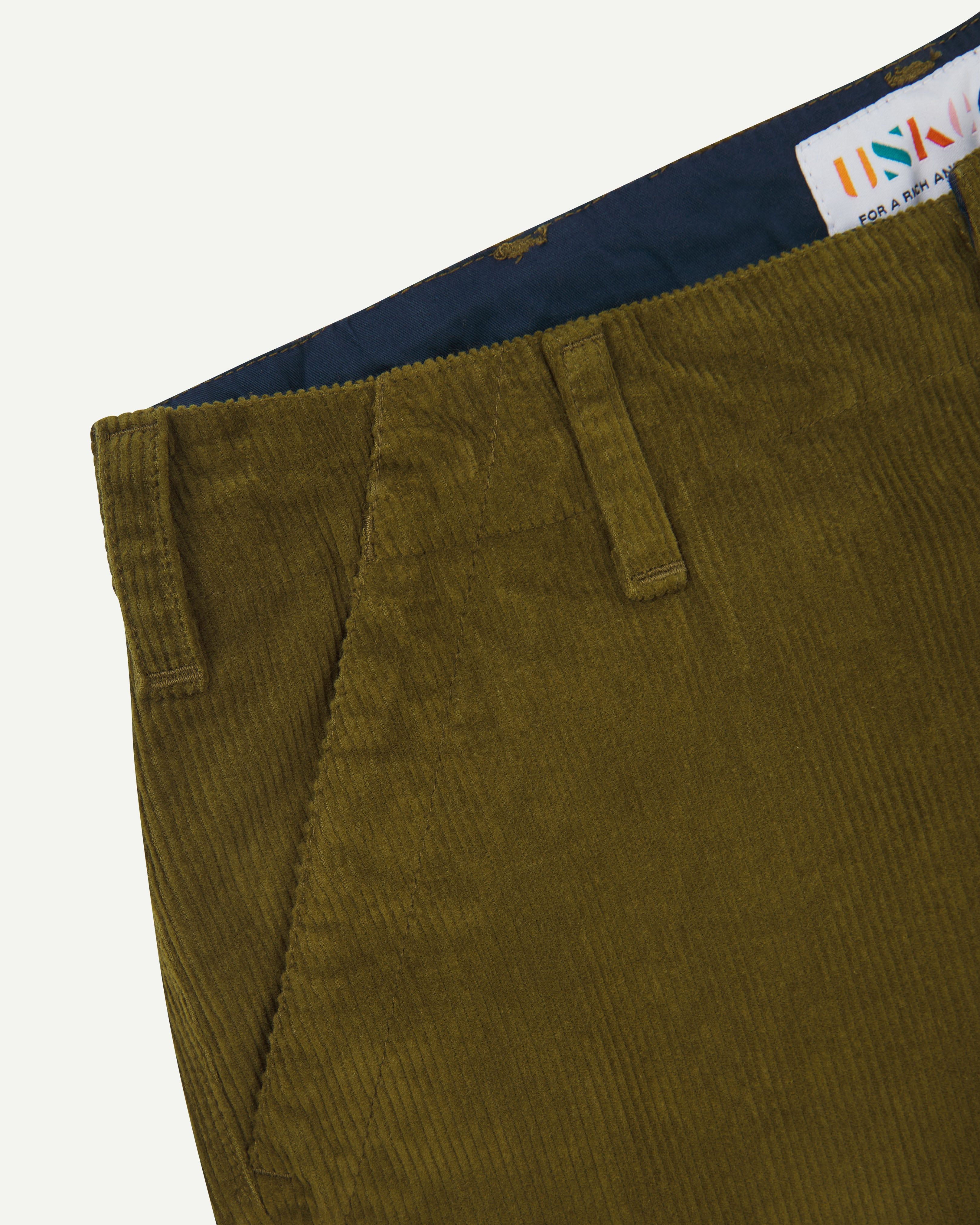 Close-up of green corduroy pants with a visible Uskees brand label on a white background