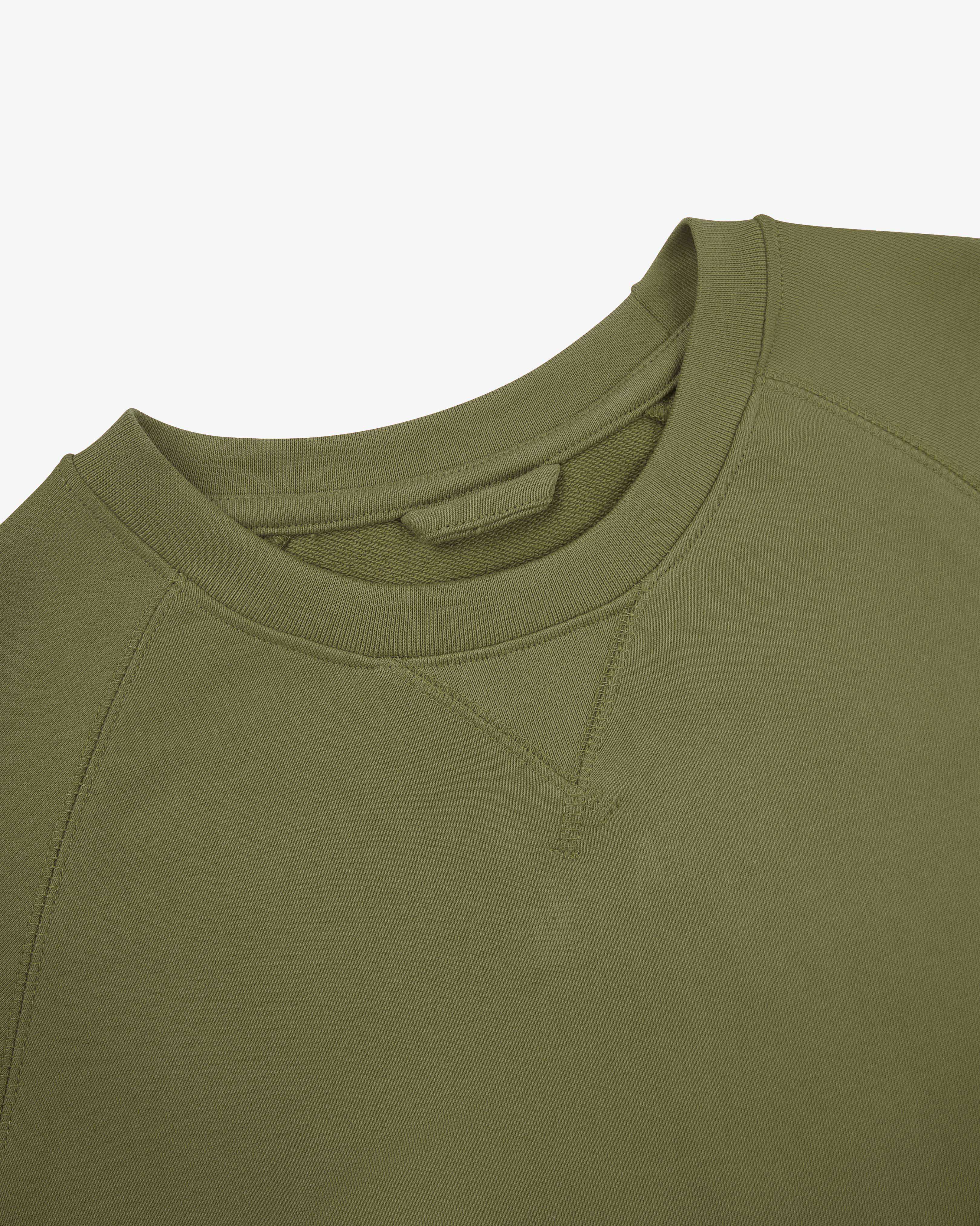 Close-up of an Uskees herb green sweatshirt on a light gray background