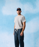 Male model wearing an Uskees baseball cap and grey marl t-shirt with blue trousers against a blue sky background 