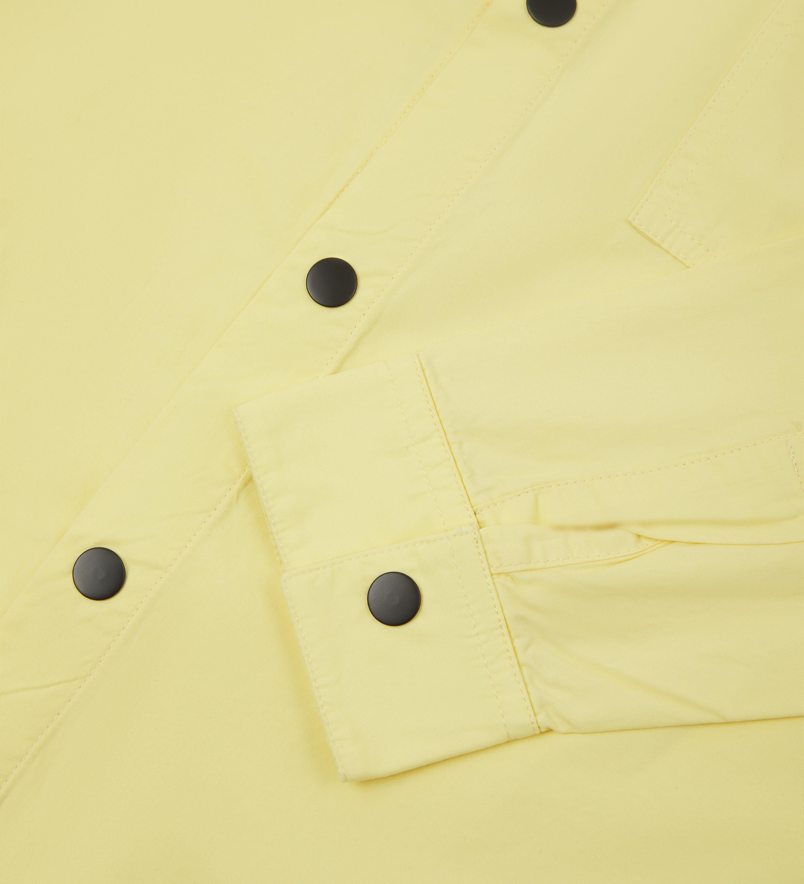 Close-up view of pale yellow buttoned lightweight overshirt from Uskees. Showing cuff and  black press studs