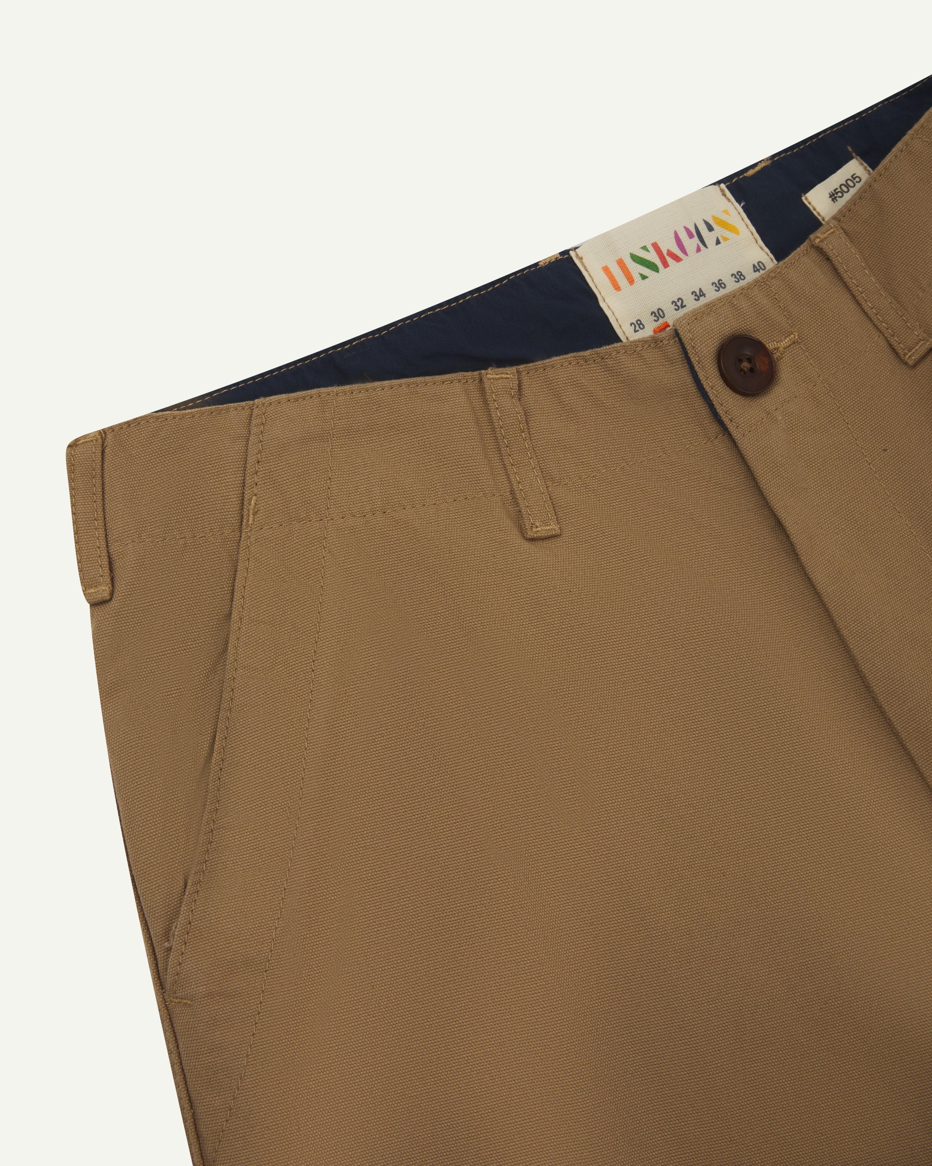 Front detail shot of #5005 Uskees men's organic cotton khaki casual trousers showing the lined waist band and size label.