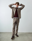 Male model wearing an Uskees light brown corduroy utility jacket, matching light brown  cord trousers, a dark maroon knit sweater, and brown leather shoes against a plain light gray studio background.