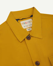 front detail view of uskees bright yellow workshirt for men showing brand label and blue yoke lining