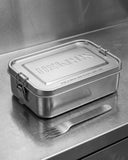 Uskees silver stainless steel location lunchbox and fork on steel countertop.