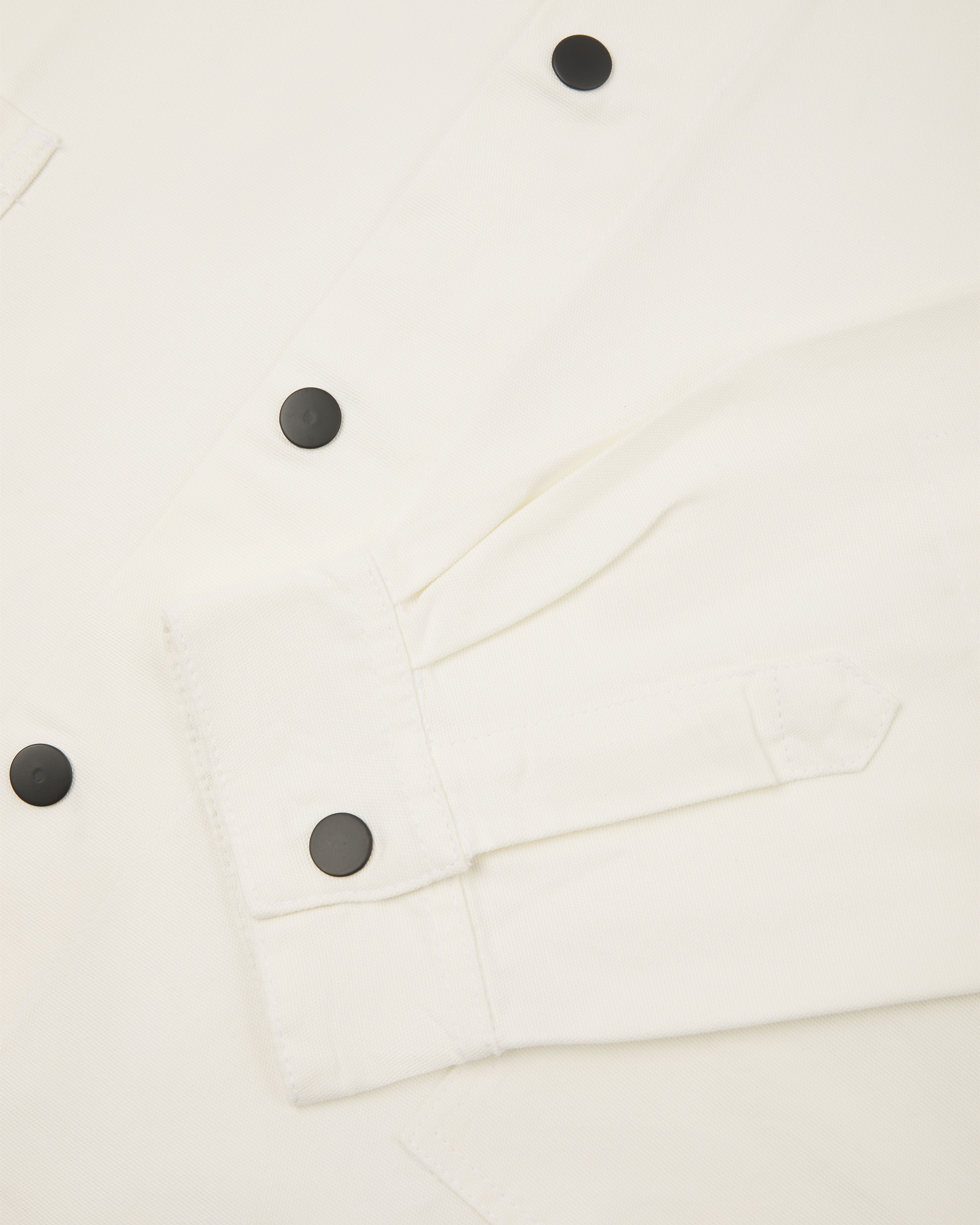 Close-up view of Uskees cream organic cotton coach jacket showing contrast black poppers on front and cuff