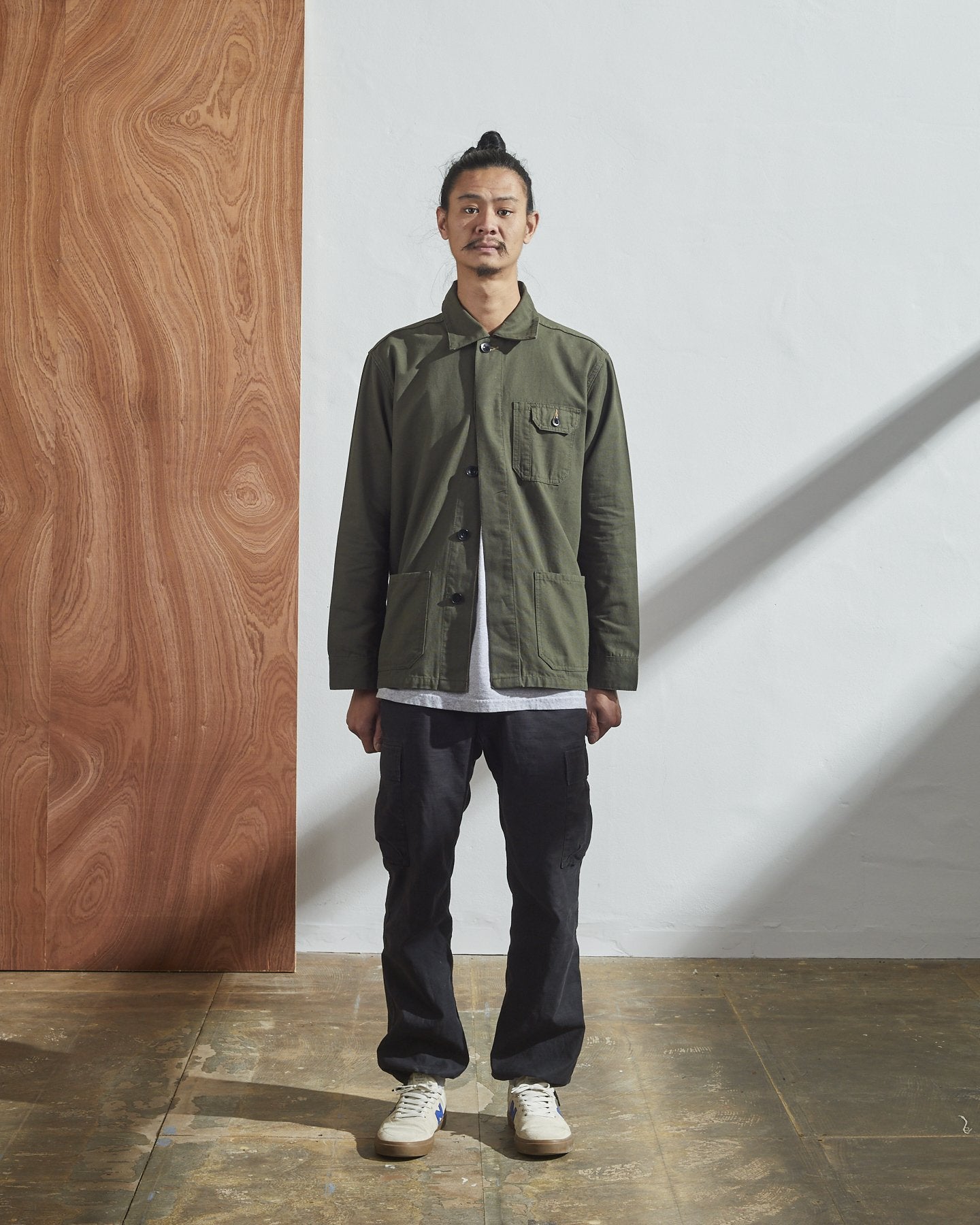 Full-length front model shot of Uskees #3011 vine green Men's overshirt with hidden front buttons. Paired with grey cargo pants.