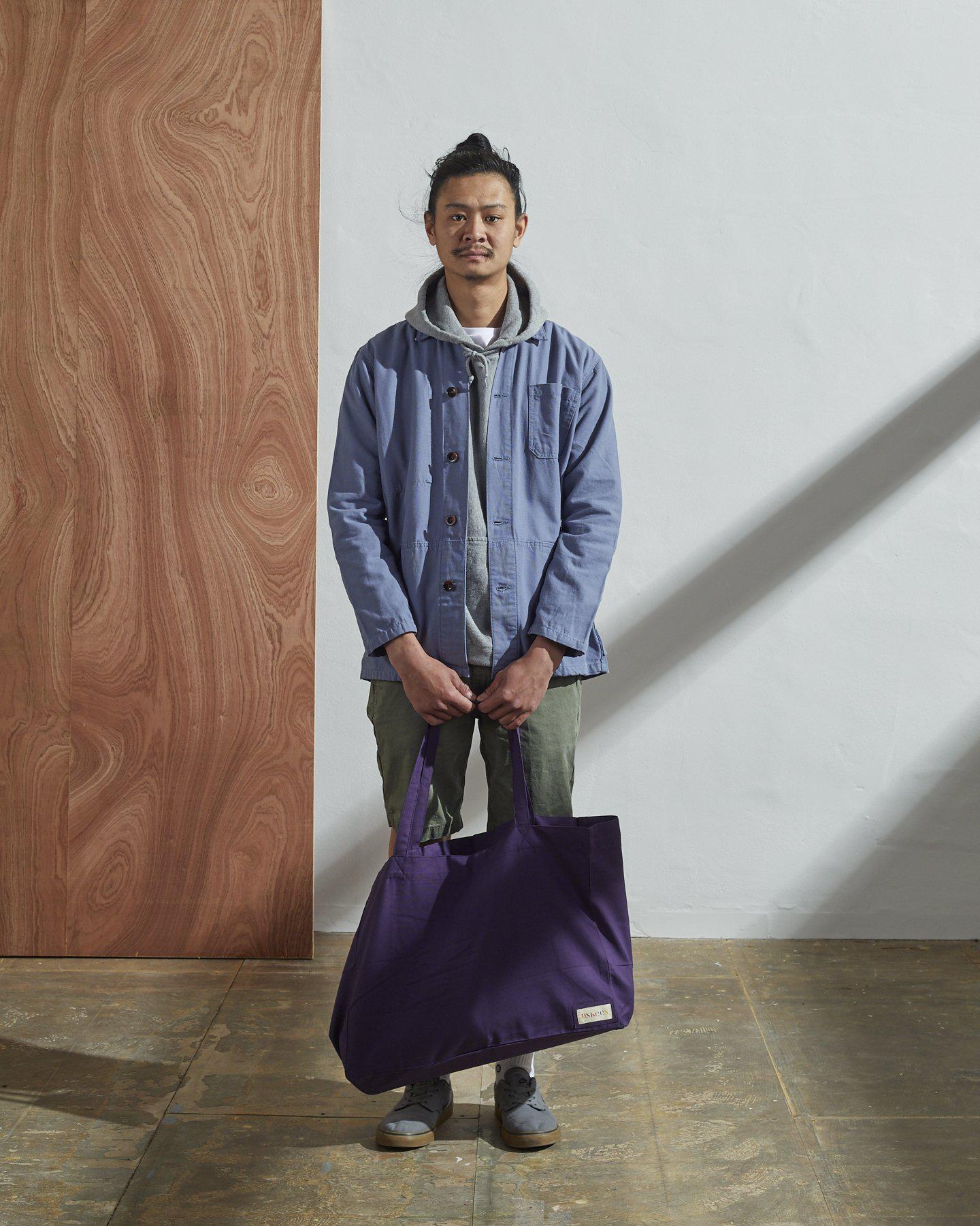 Full-length, front-view of model holding Uskees #4001, large purple tote bag. Paired with light blue jacket.
