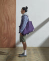 Full-length, side-view of model carrying Uskees #4001, large purple tote bag over left shoulder.