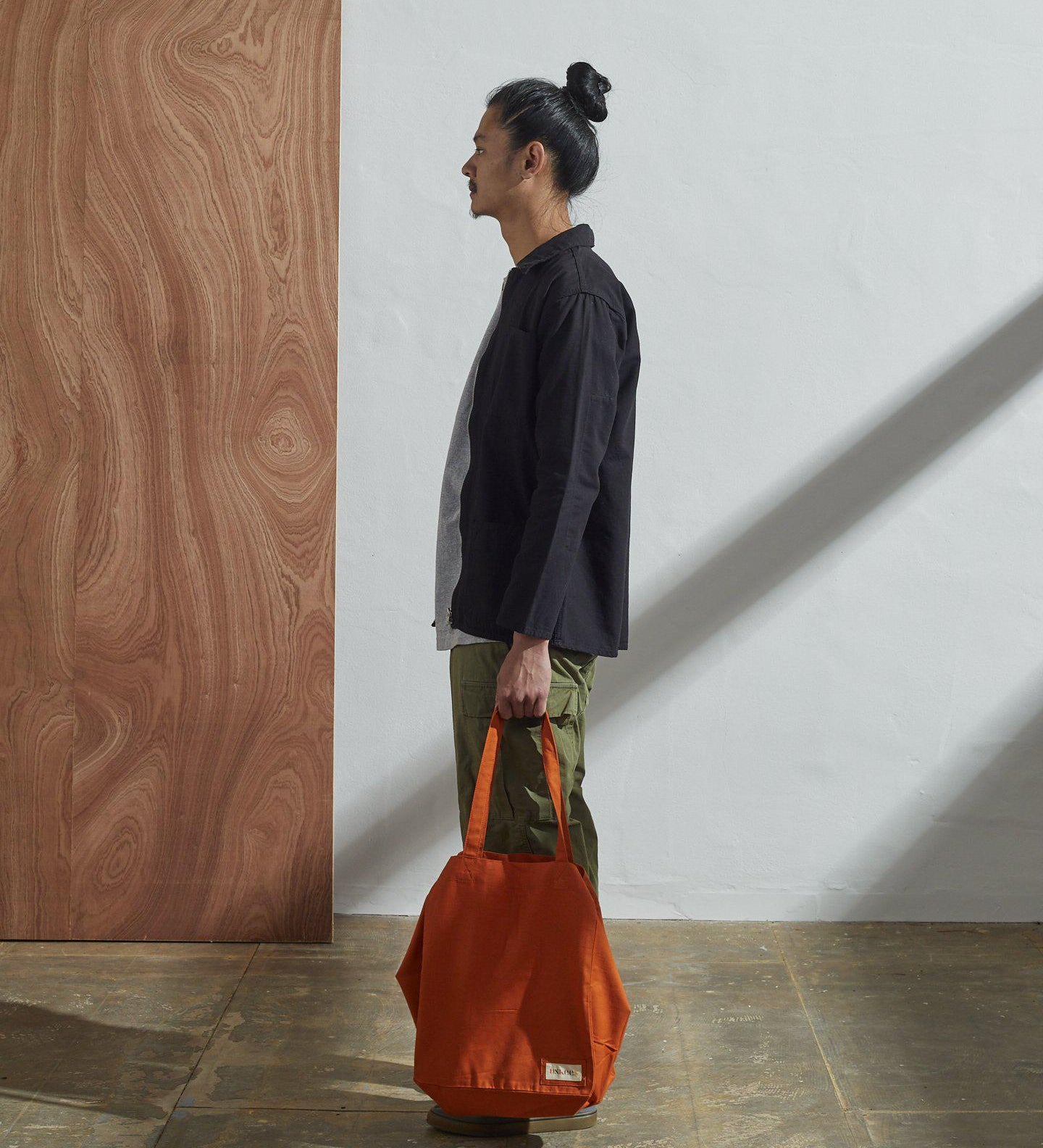 Full-length, side-view of model holding Uskees #4002, small golden-orange tote bag.