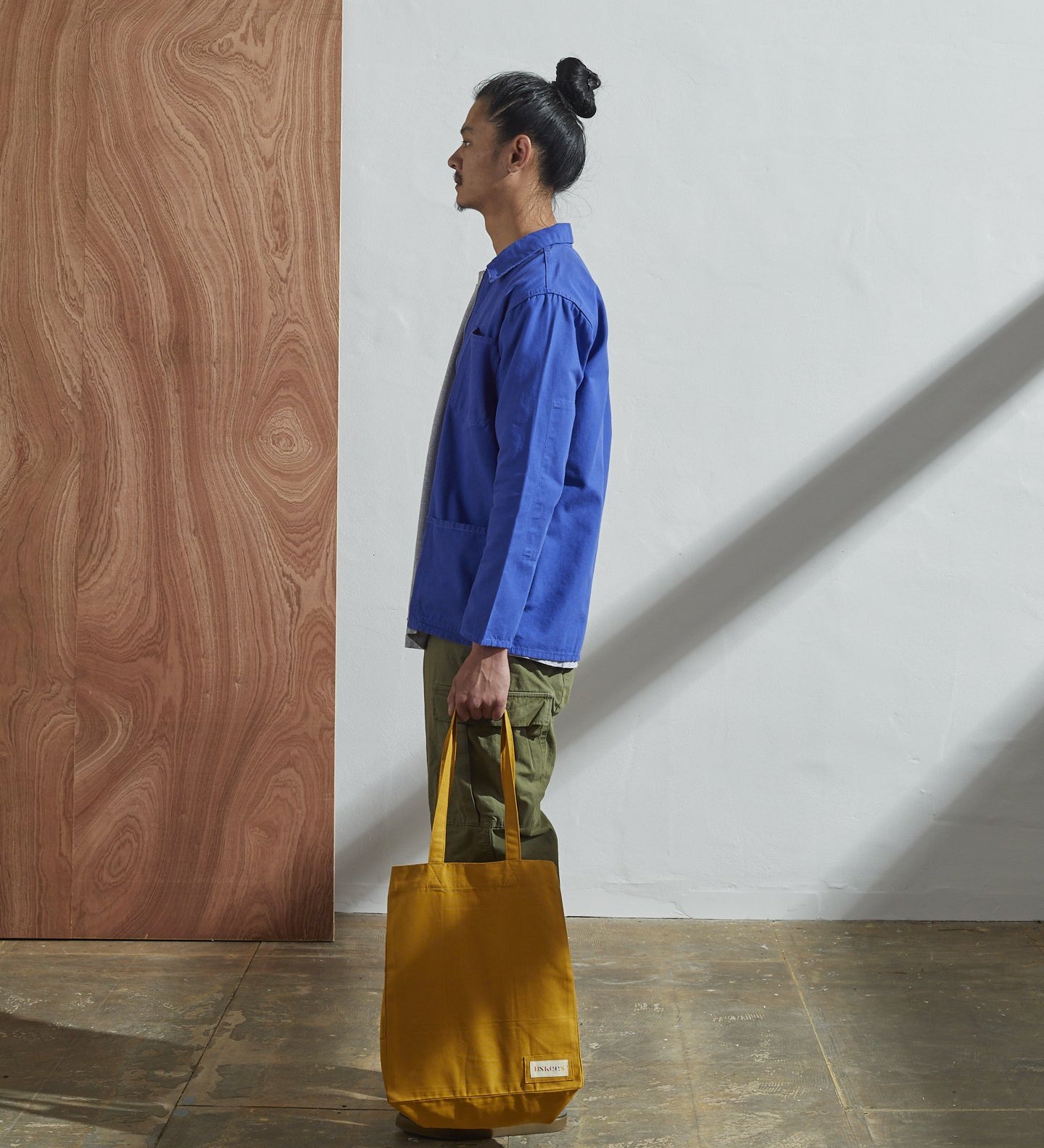Full-length, side-view of model holding Uskees #4002, small yellow tote bag.