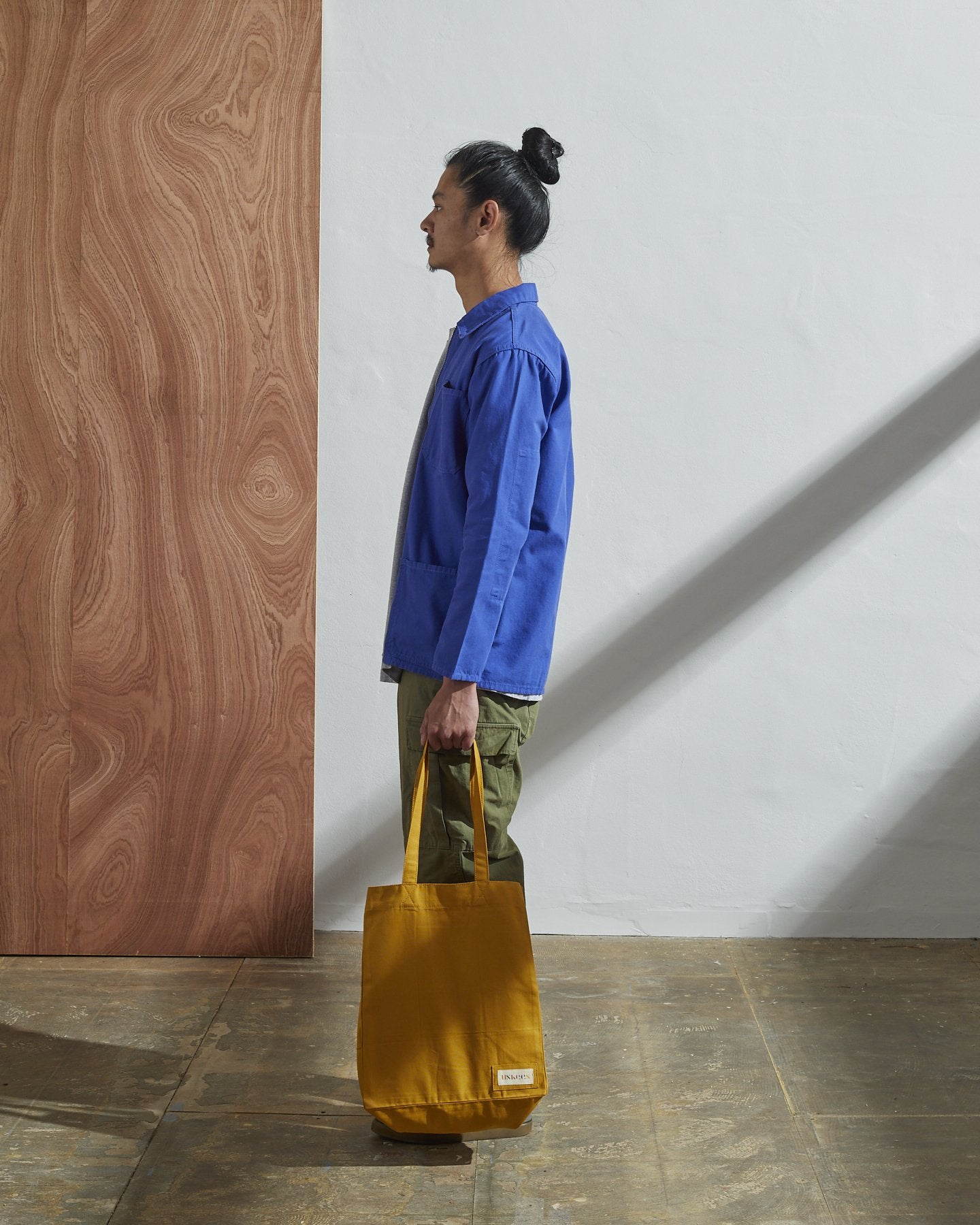 Full-length, side-view of model holding Uskees #4002, small yellow tote bag.
