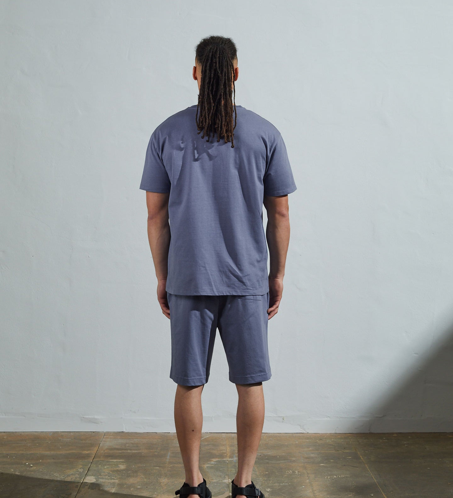 Full-length back view of model wearing teal, relaxed cut organic cotton #7006 jersey T-shirt by Uskees paired with matching #7007 shorts.