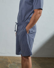 Side view of model wearing teal organic cotton #7007 jersey shorts by Uskees with hands in side pockets.