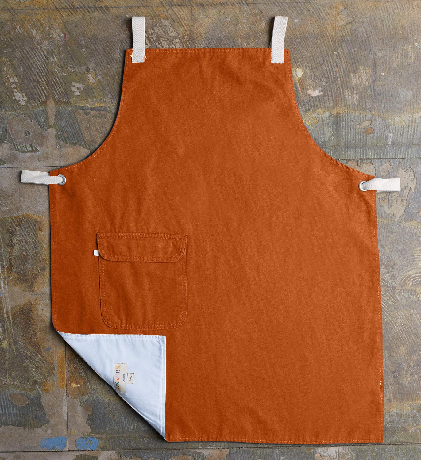 Full, flat view of gold-orange #9001 work apron with hip pocket by Uskees. Left corner folded up to reveal lining and 'Uskees' label.