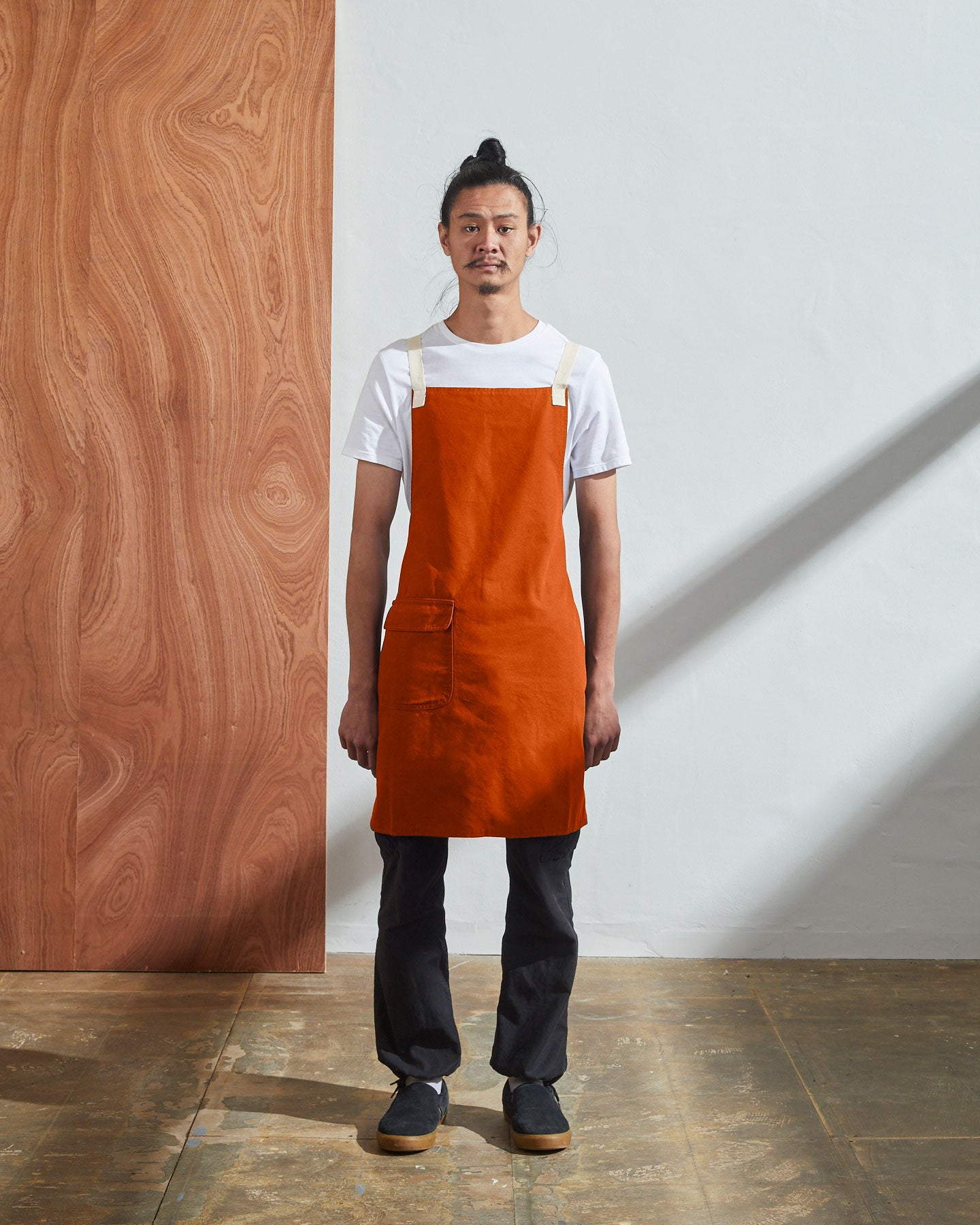 Full-length, front view of male model wearing Uskees #9001 gold work apron by Uskees. Showing convenient hip pocket and contrasting cream straps.